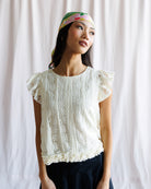 Woman wearing a white lace top and colorful headband against a plain background