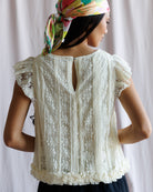 Woman wearing a white lace top with a colorful headscarf on a plain background