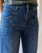 Close-up of a person wearing blue denim jeans with a slightly faded wash, showing the front waistband, belt loops, and side pockets.