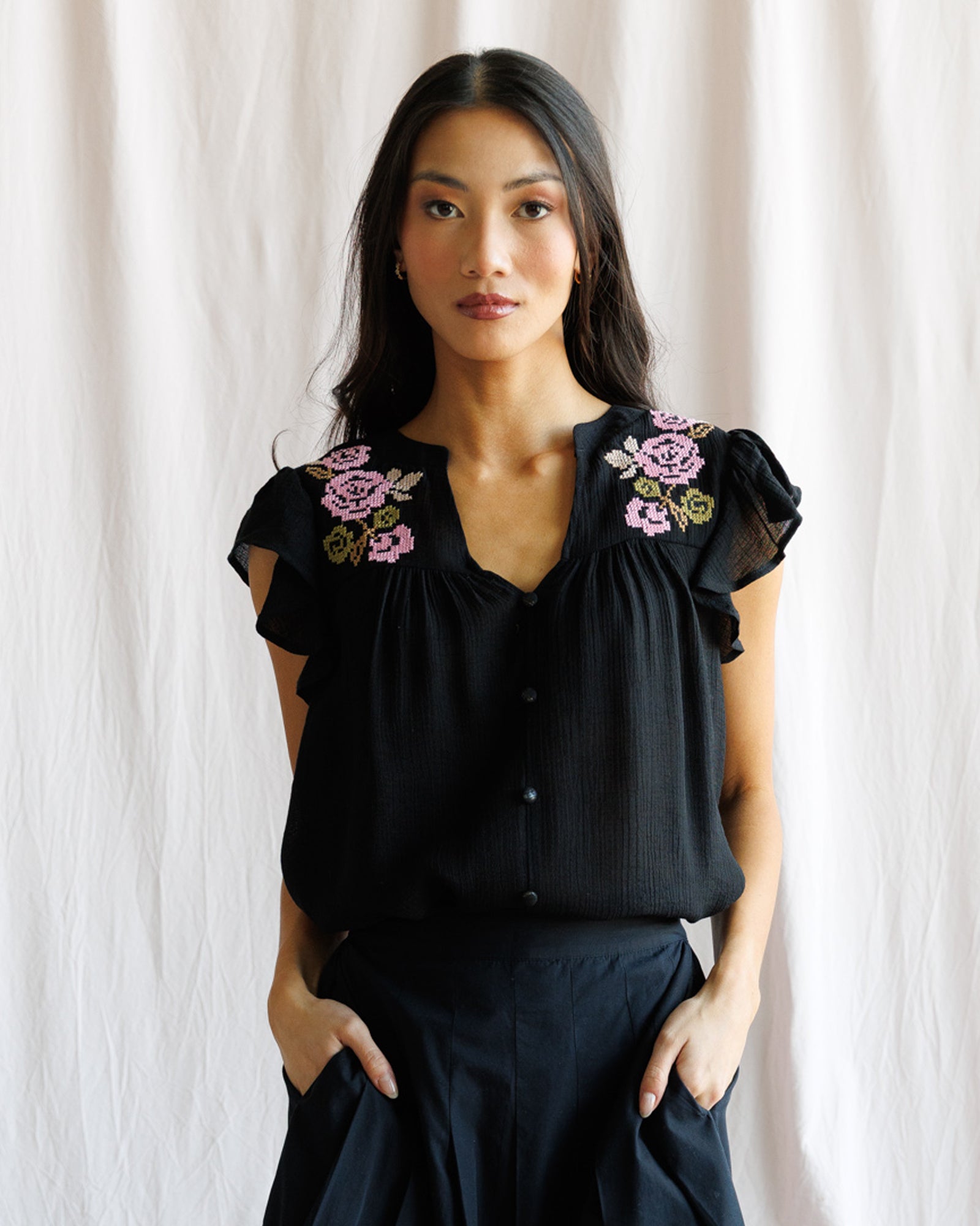 Woman wearing a black blouse with floral embroidery against a white curtain background