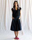 Woman wearing a black blouse with floral embroidery and a black skirt against a white background