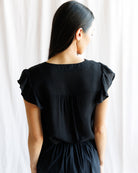 Woman wearing a black dress with ruffled sleeves against a white curtain background