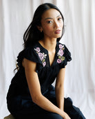Woman wearing a blacktop with floral embroidery against a white curtain background