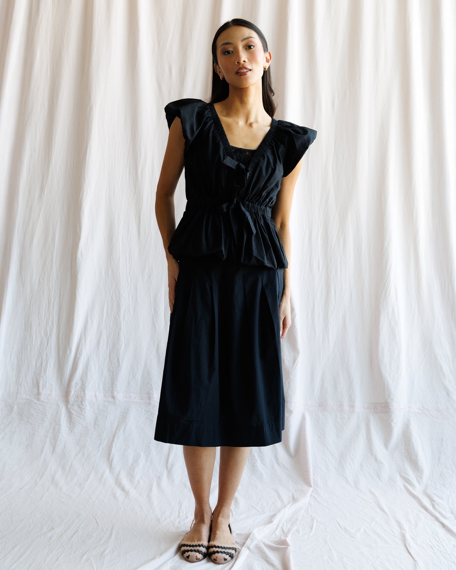 Woman wearing a black blouse and matching skirt against a white background