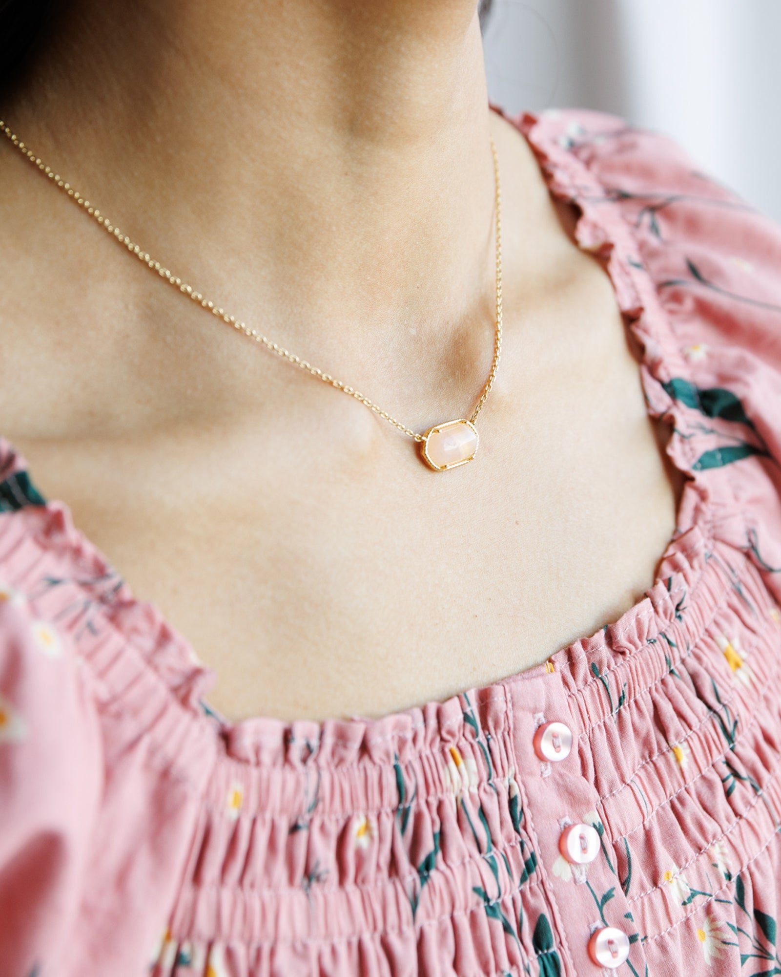 Gold necklace with a heart pendant worn by a person in a pink floral dress.