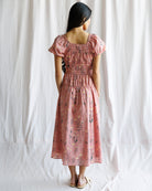 Woman wearing a pink floral dress against a white curtain background