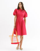 Woman wearing a red checkered dress holding a tote bag with text on a white background