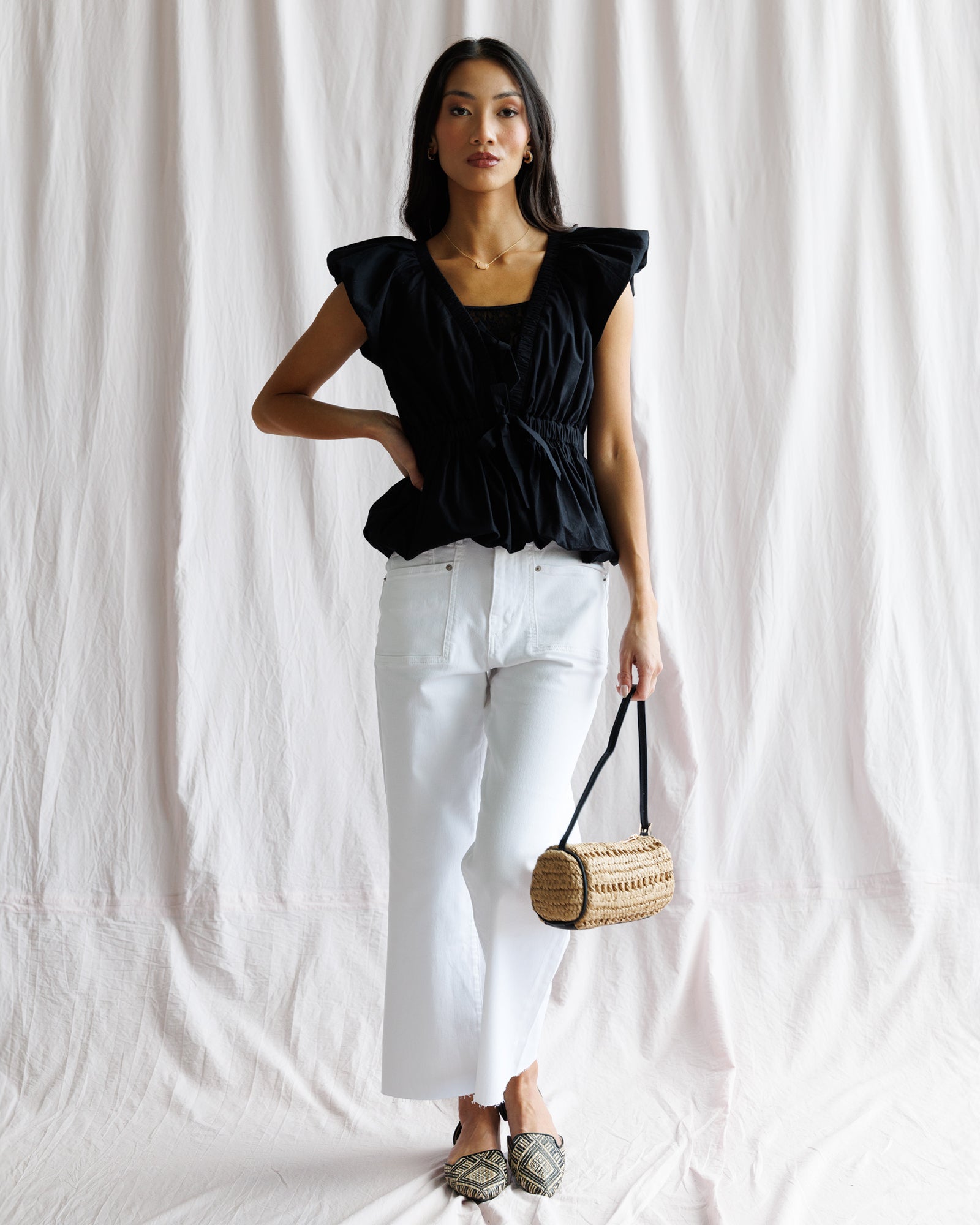 Woman wearing a black top and white pants holding a wooden handbag against a white background