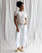 Woman wearing a white blouse and white pants against a white curtain background