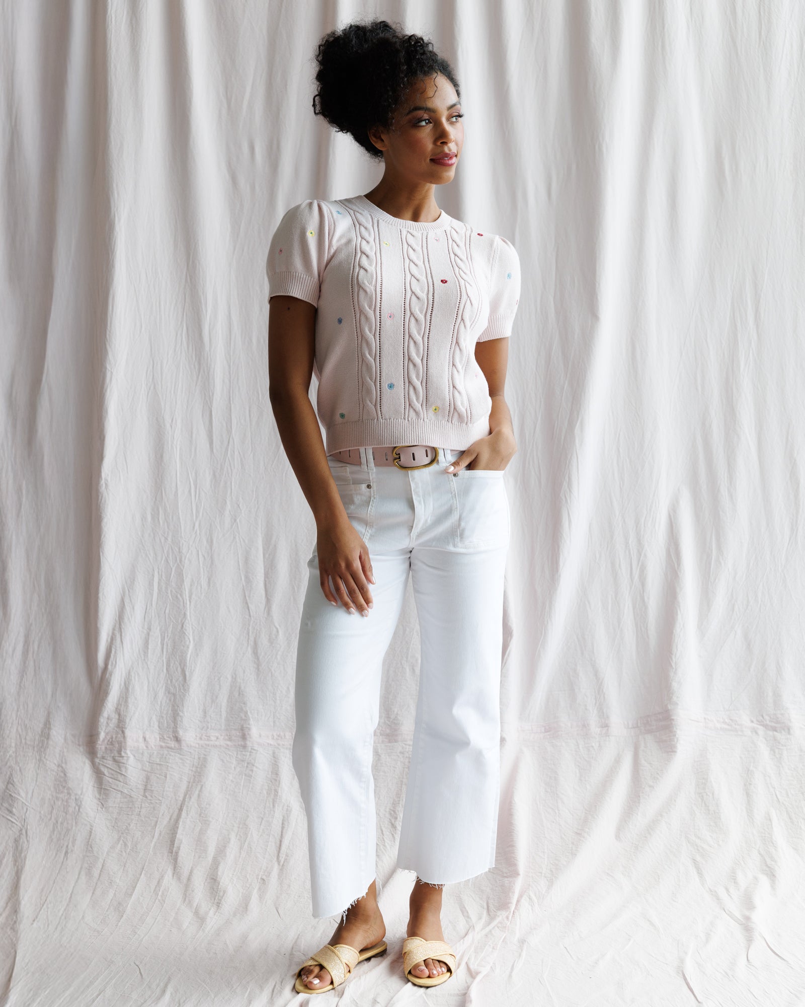 Woman wearing a white blouse and white pants against a white curtain background