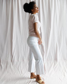 Woman wearing a white shirt and light blue jeans against a white curtain background