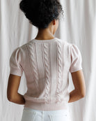 Person wearing a light pink knitted sweater with cable patterns against a white background