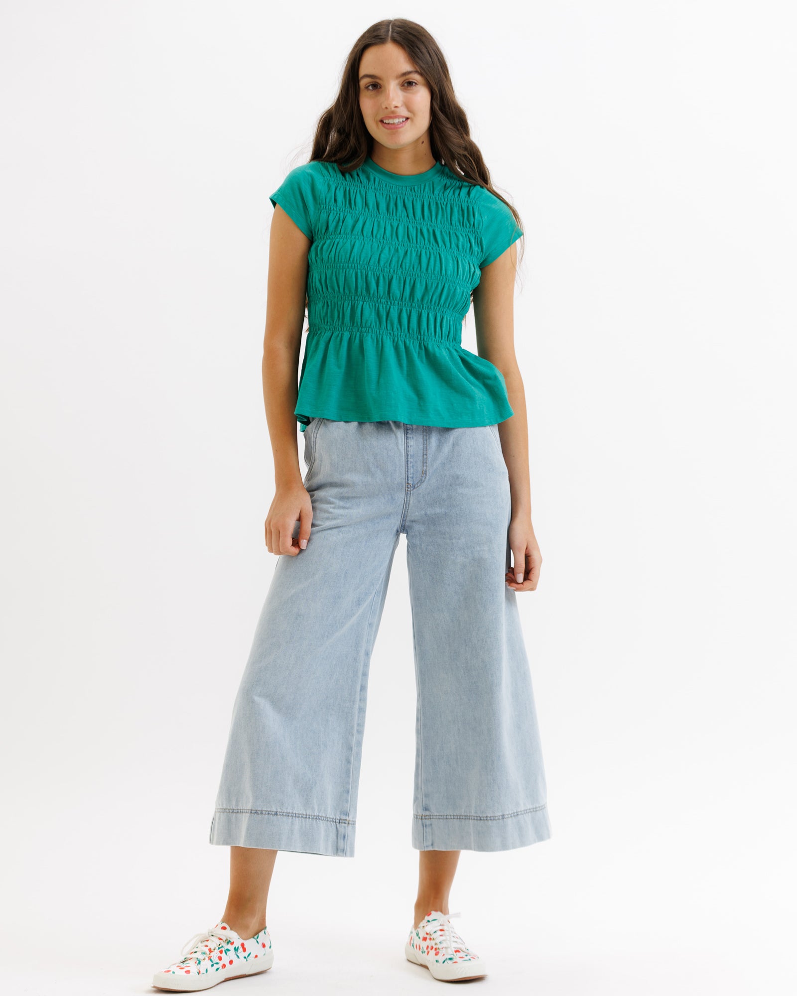 Woman wearing a green top and light blue jeans on a white background