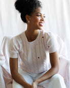 Woman wearing a white sweater with colorful buttons sitting on a white couch.