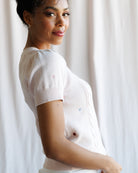 Woman wearing a white sweater against a light curtain background
