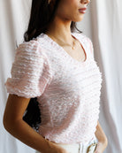 Woman wearing a light pink textured blouse against a neutral background