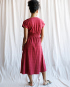 Person wearing a red dress standing against a white curtain