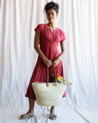 Woman in a red dress holding a straw bag with flowers against a white background