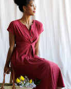 Woman in a red dress sitting with flowers against a white curtain