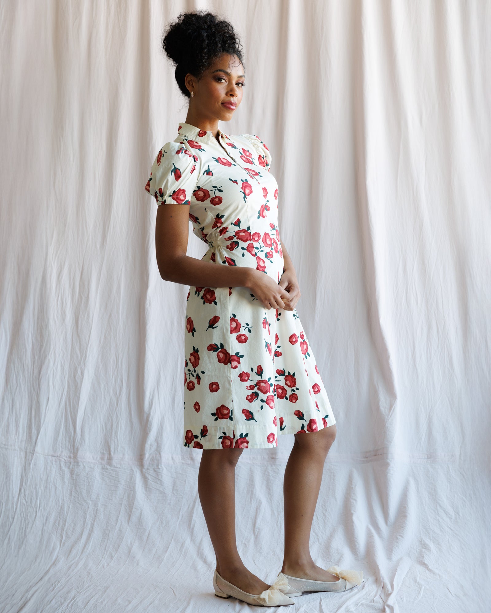 Woman wearing a floral dress standing against a plain background