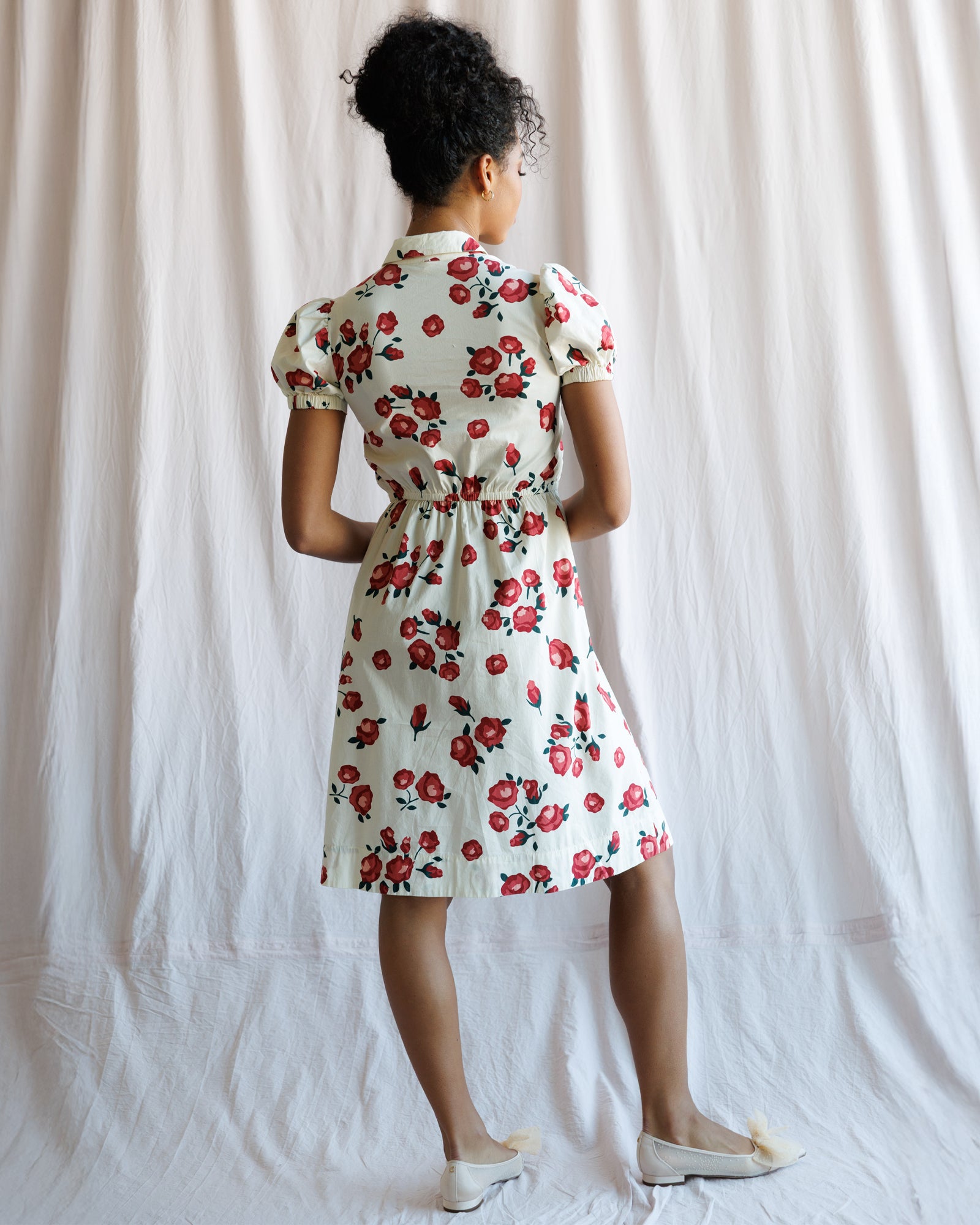 Woman wearing a floral dress standing against a plain background