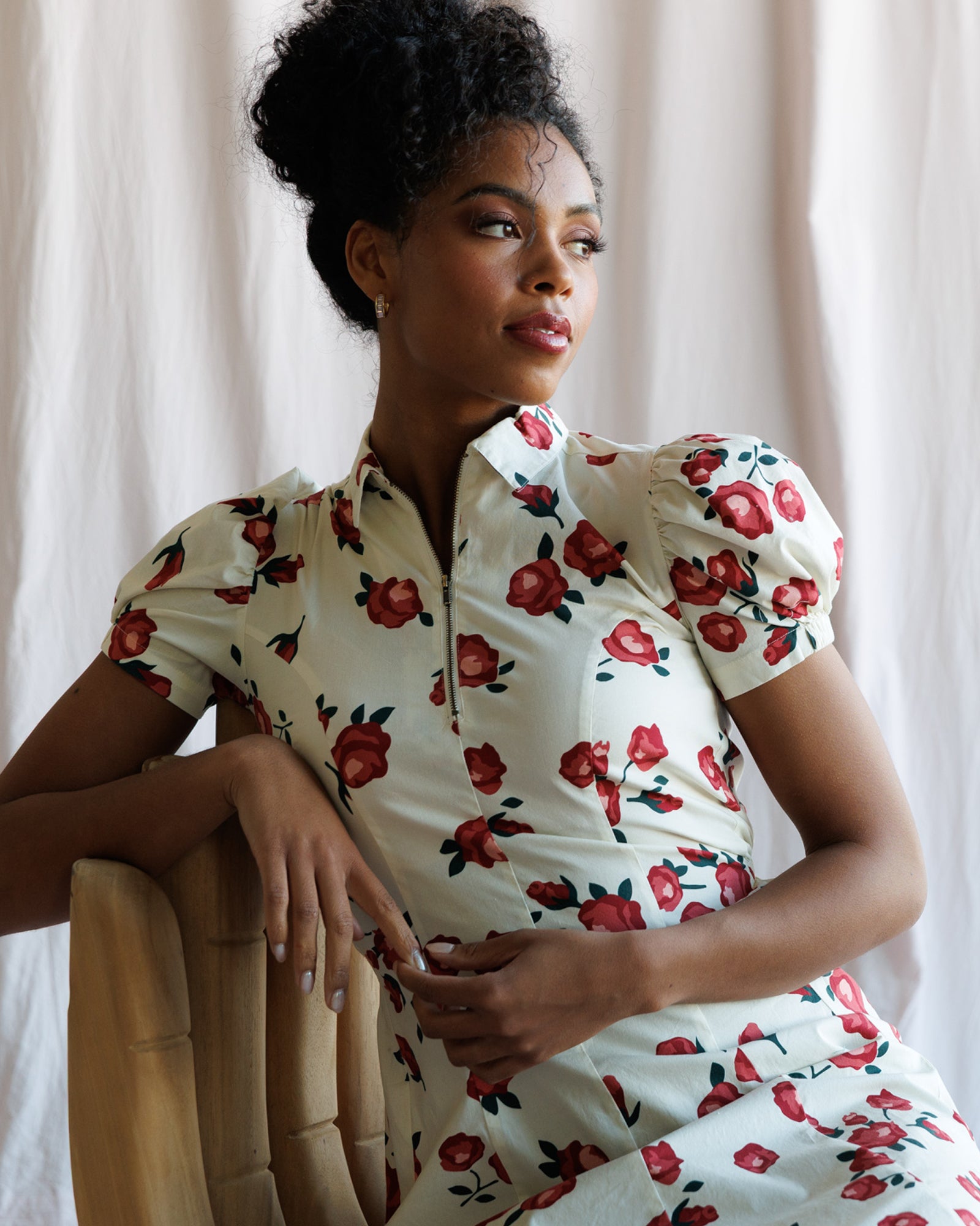 Woman wearing a floral dress sitting against a white curtain