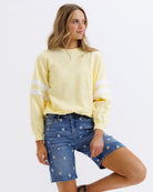 Woman wearing a light yellow sweatshirt with white stripes and denim shorts on a white background