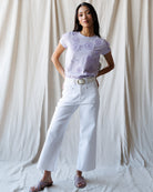 Woman wearing a light purple floral top and white pants against a plain background