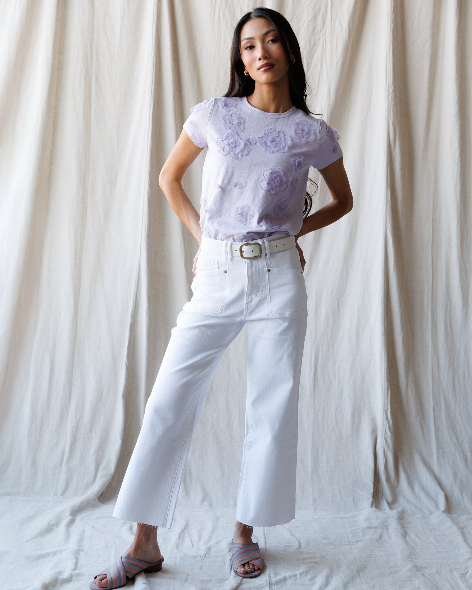 Woman wearing a light purple floral top and white pants against a plain background
