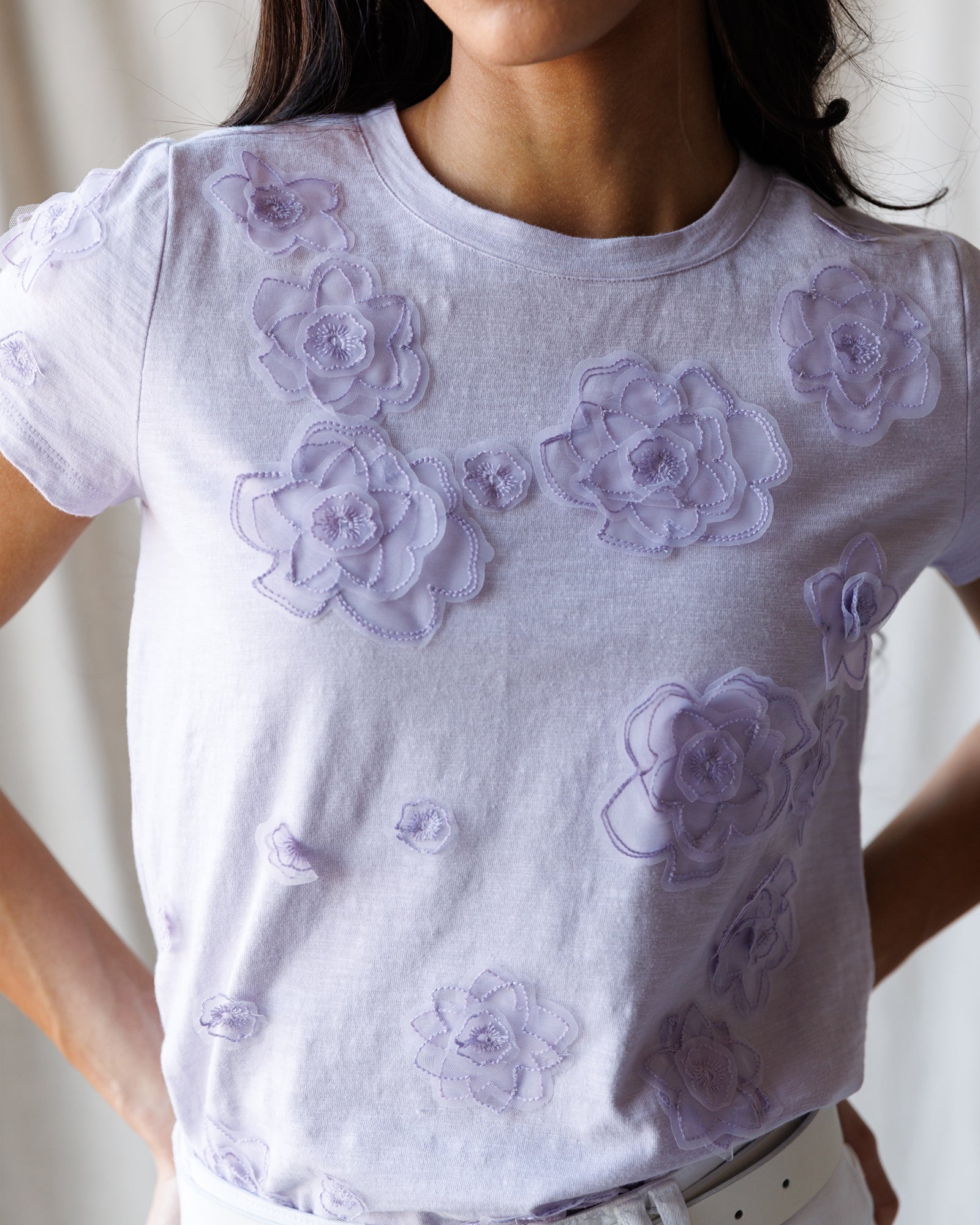 White t-shirt with purple floral designs worn by a person against a neutral background