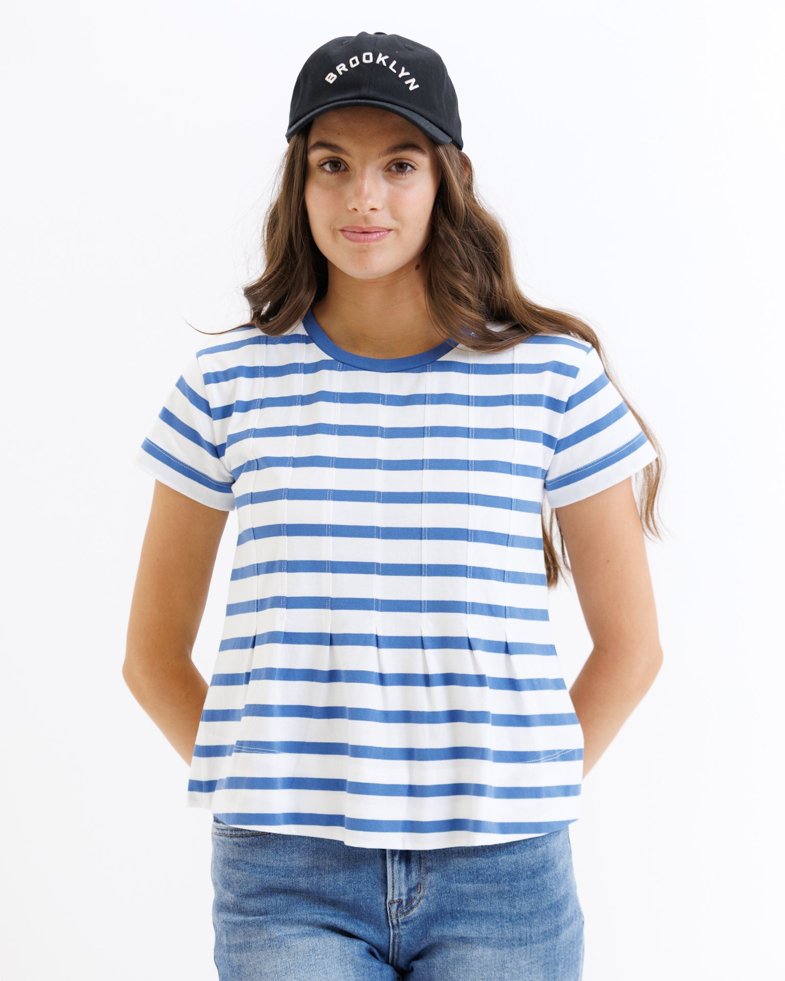 Woman wearing a blue and white striped t-shirt with a black cap on a white background