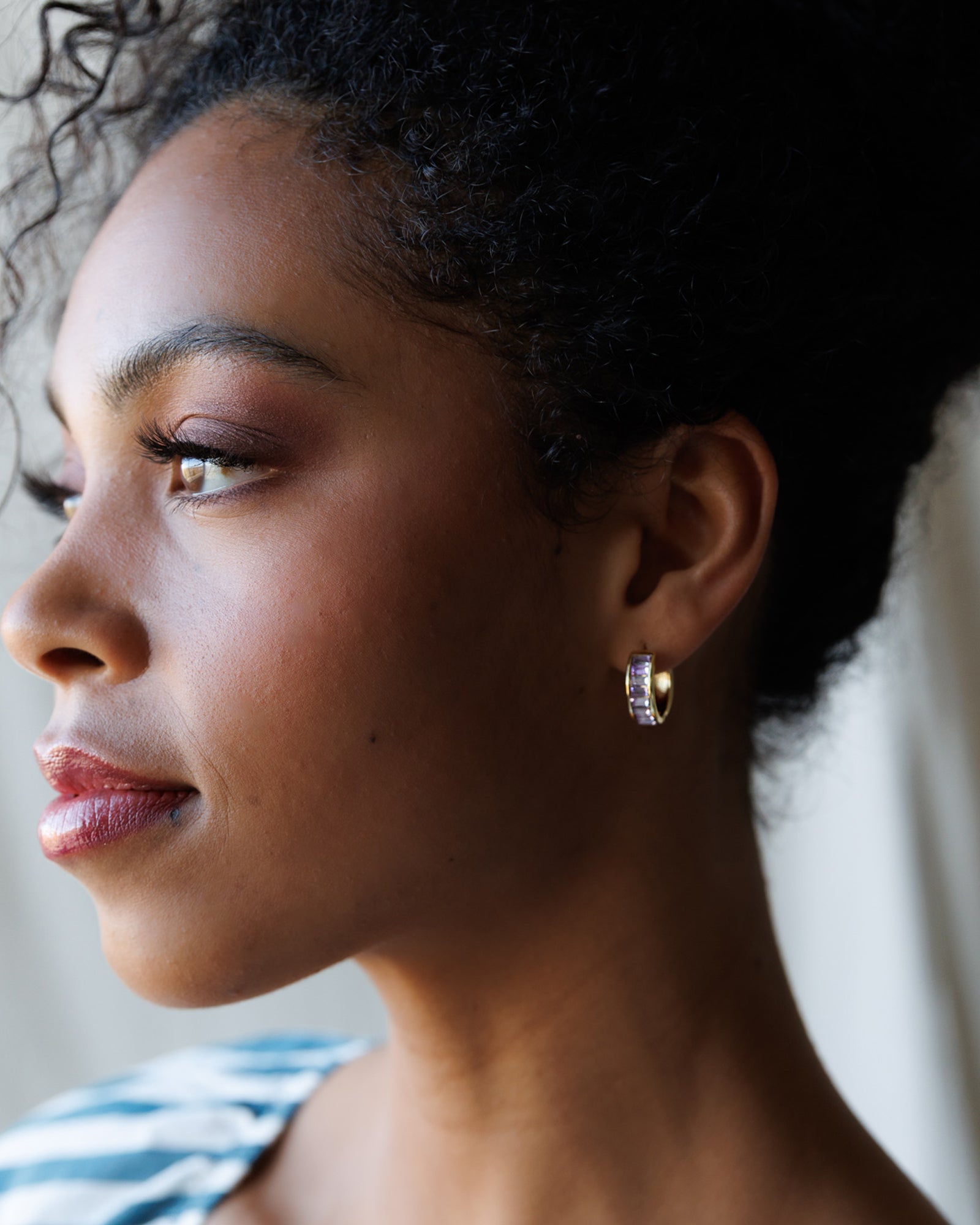 Close-up of a woman wearing gold hoop earrings with a blurred background