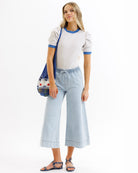 Woman wearing a striped shirt and light blue jeans, holding a colorful bag on a white background