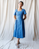 Woman wearing a blue dress standing against a white curtain backdrop