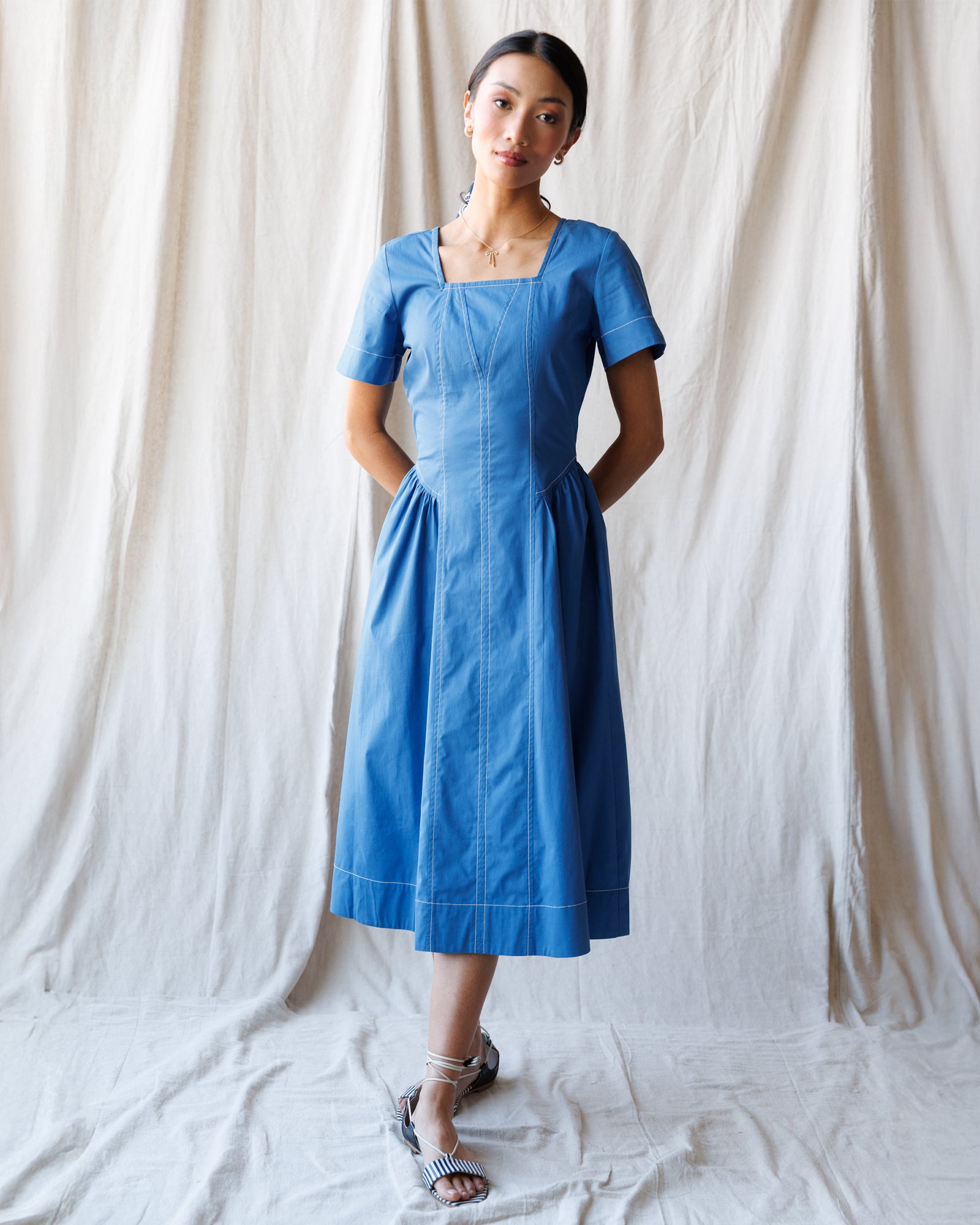 Woman wearing a blue dress standing against a white curtain backdrop