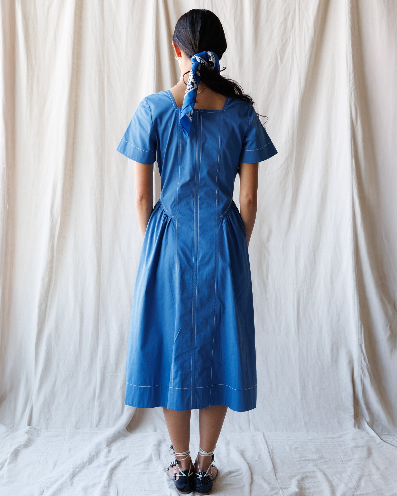 Person wearing a blue dress standing against a white curtain