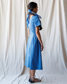 Woman wearing a blue dress with a white curtain background