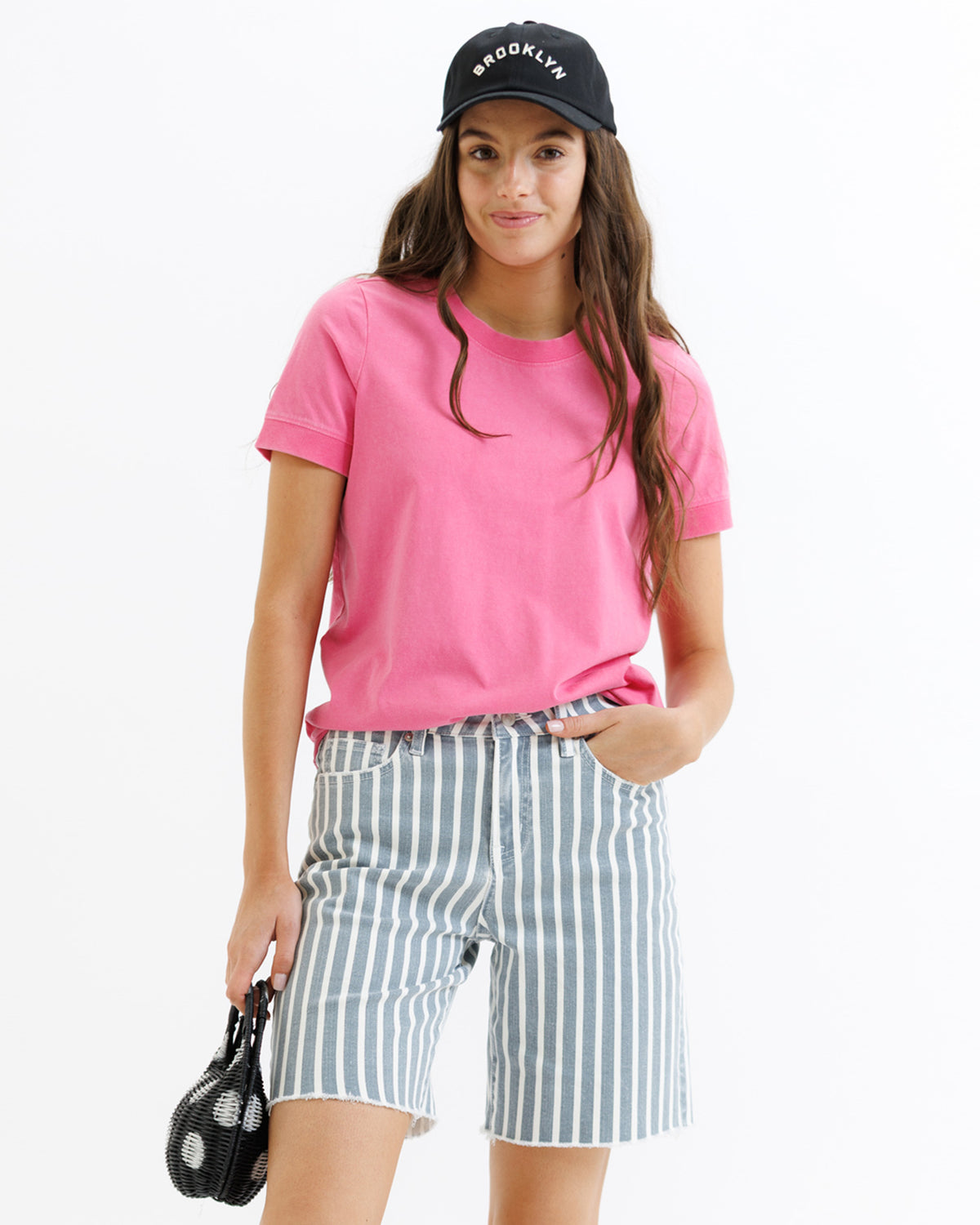 Woman wearing a pink t-shirt, striped shorts, and a black cap with 'Brooklyn' text on a white background
