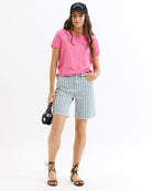 Woman wearing a pink t-shirt, striped shorts, and a black cap on a white background