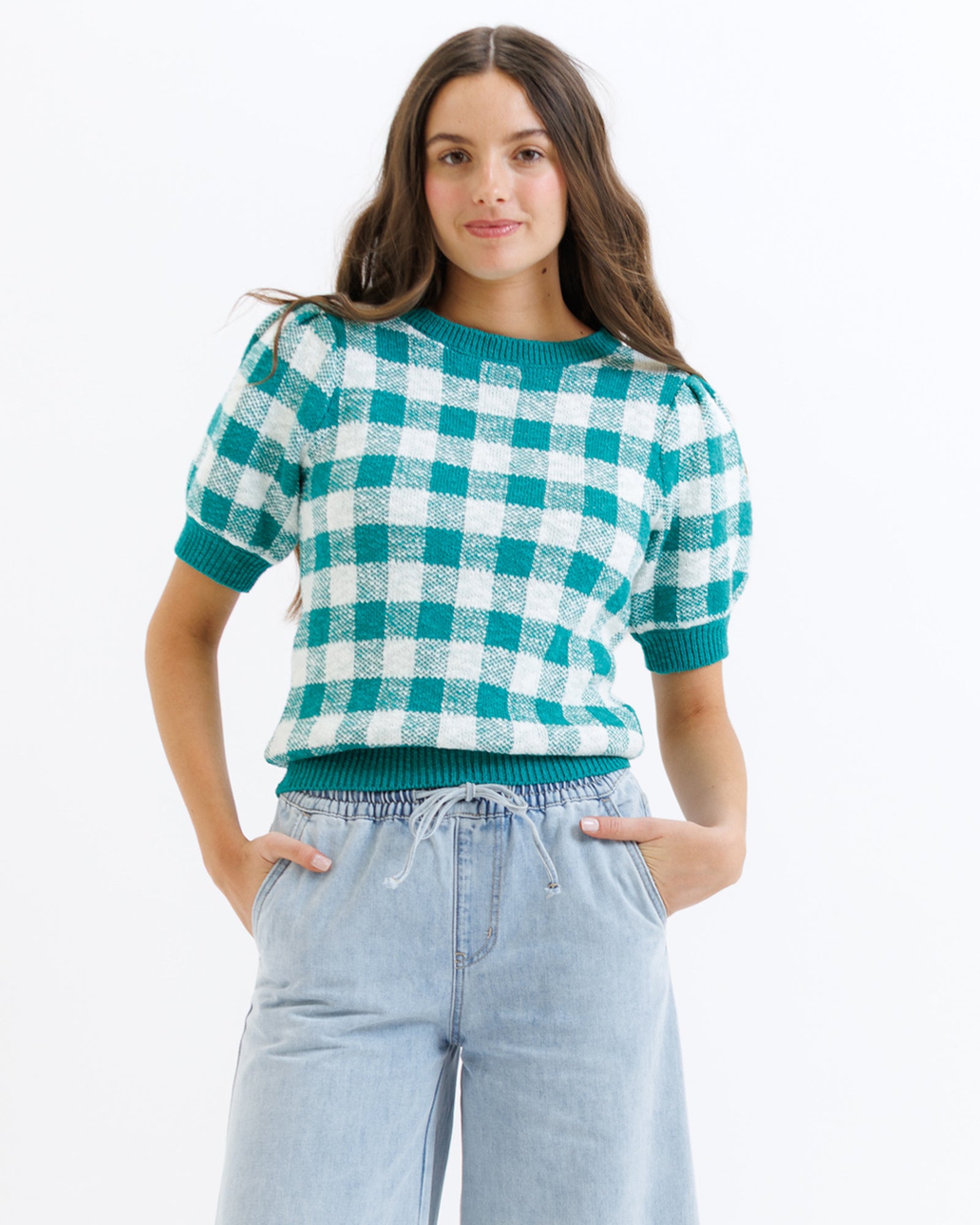Woman wearing a green and white checkered sweater with light blue jeans on a white background