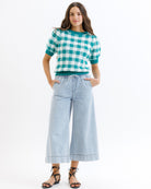 Woman wearing a green and white checkered shirt with light blue jeans on a white background