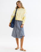 Woman wearing a yellow sweatshirt and blue checkered skirt with a blue bag on a white background