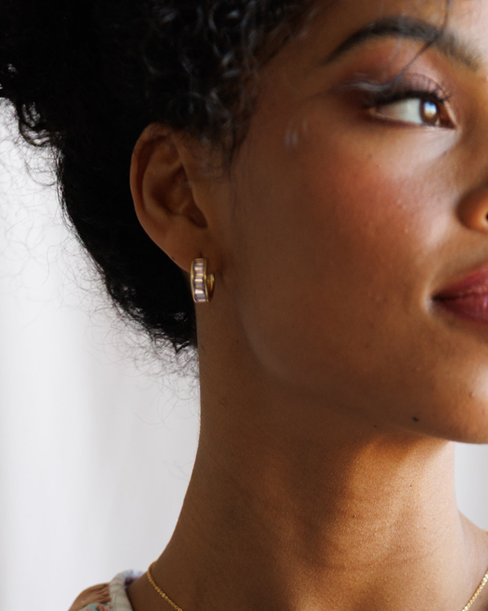 Close-up of a person wearing gold hoop earrings with a neutral background