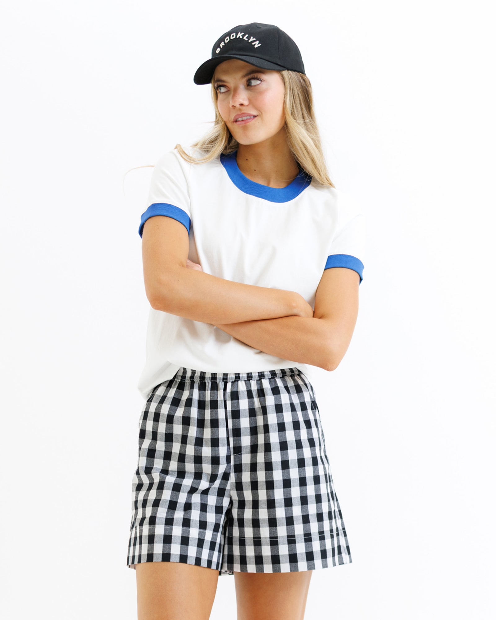 Woman wearing a white t-shirt with blue trim, black cap, and checkered shorts on a white background