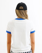 Person wearing a white t-shirt with blue accents and a black cap on a white background