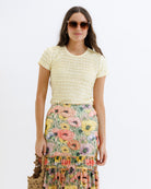 Woman wearing a yellow top and floral skirt on a white background
