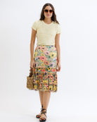 Woman wearing a yellow top and floral skirt on a white background