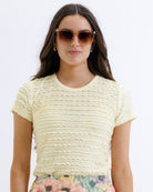 Woman wearing a yellow textured top and floral pants on a white background