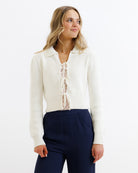 Woman wearing a white cardigan over a lace top with navy pants on a white background
