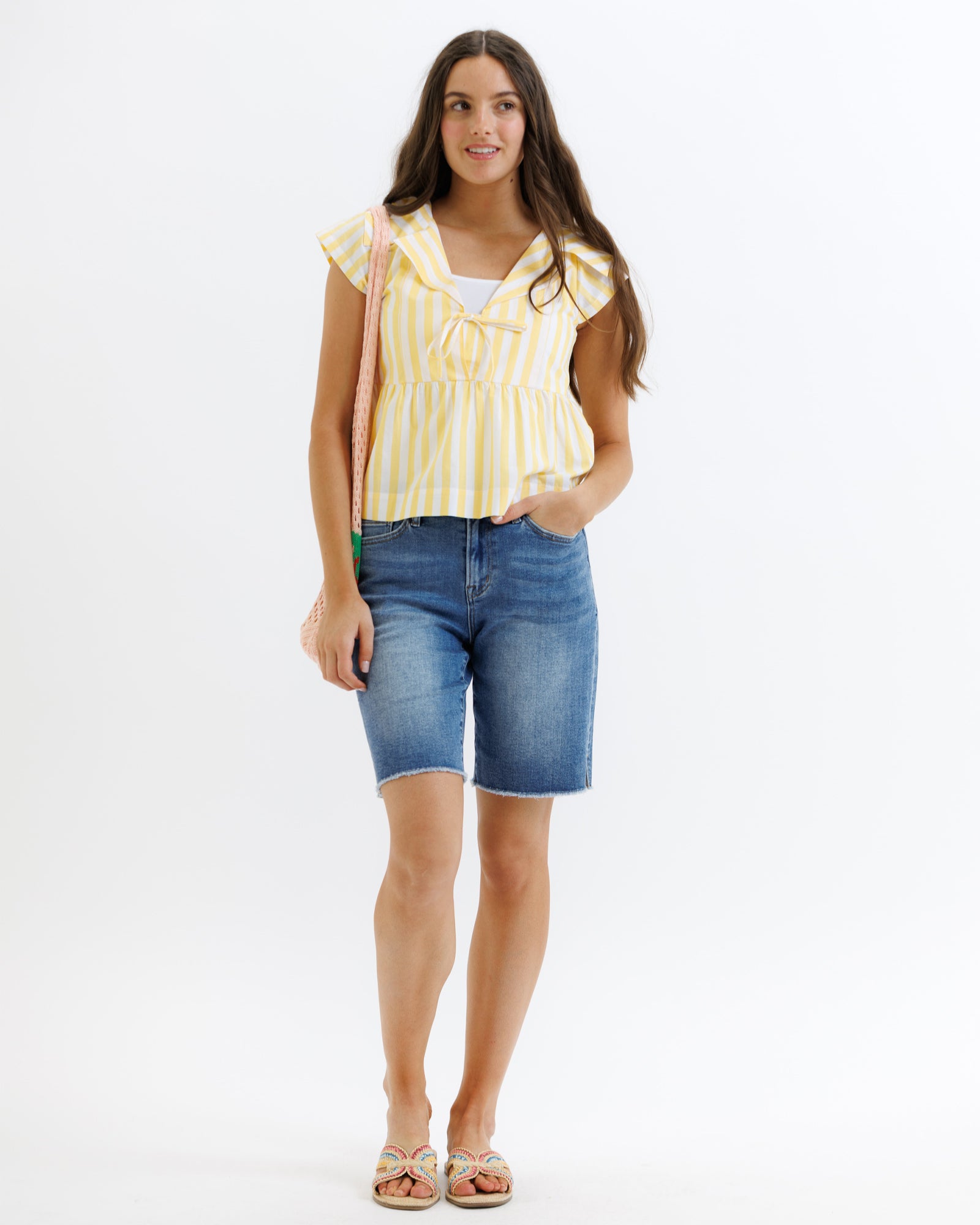 Woman wearing a yellow striped top and blue denim shorts on a white background